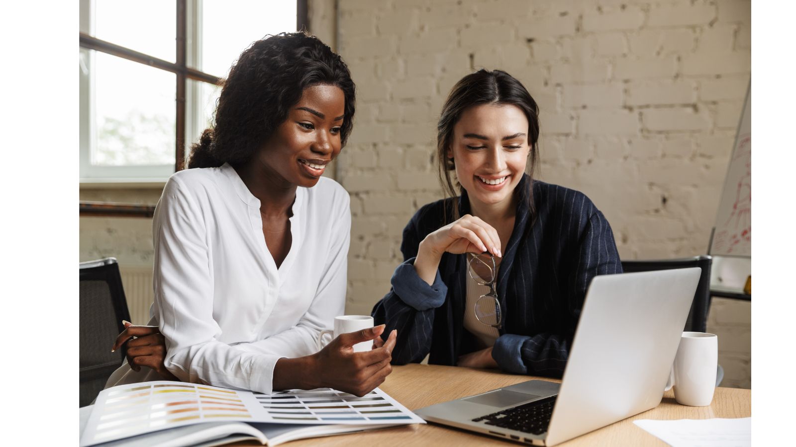 Two colleagues smiling and reviewing a laptop together at a desk