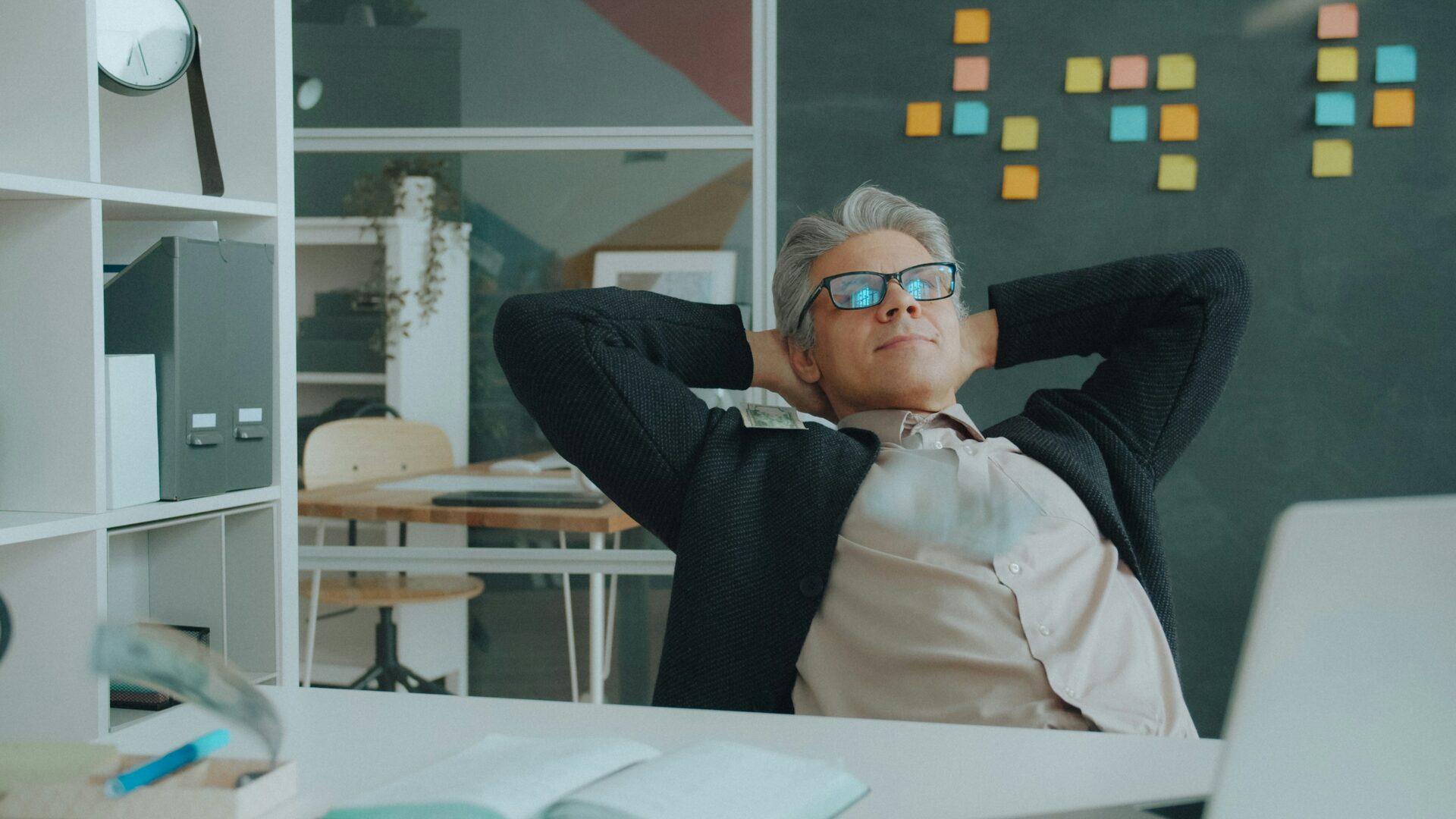 A business owner leaning back in his chair with hands behind his head, relaxed at his desk